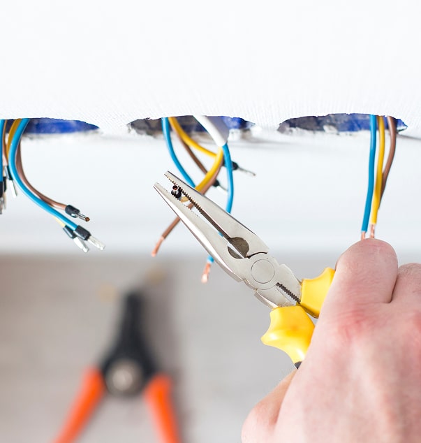 Câblage électrique facile : les outils de l'électricien. Électricien tenant une pince pour manipuler des fils de cuivre dénudés lors d'une installation électrique. Câblage sortant d'une cloison blanche.