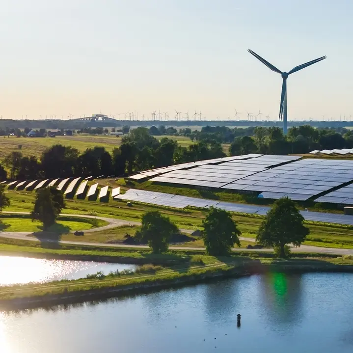 Énergie Solaire et Éolienne : l'Avenir du Renouvelable. Vaste parc solaire photovoltaïque près d'un étang, avec une grande éolienne et des dizaines de turbines sur l'horizon, illustrant l'énergie renouvelable.